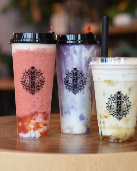 Three cups of flavored boba tea rest on small wooden table.