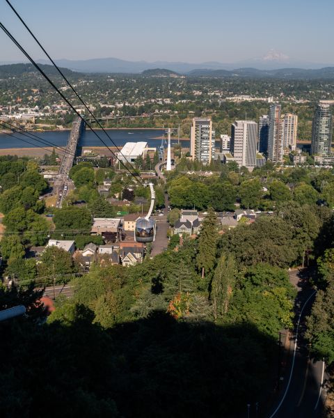 city view of buildings along a river and several bridges as seen from the top landing of an aerial tram