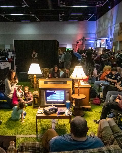 gamers and onlookers gather around a vintage television set in a living room set up at a gamer conference in Portland, Oregon