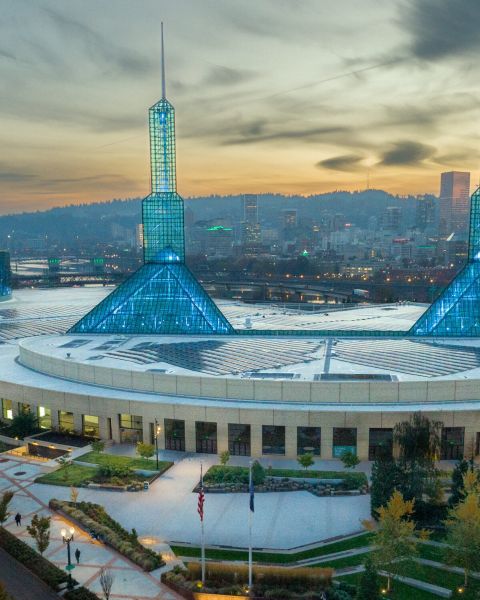 a vast building with two spires at sunset with the city skyline and hills in the background