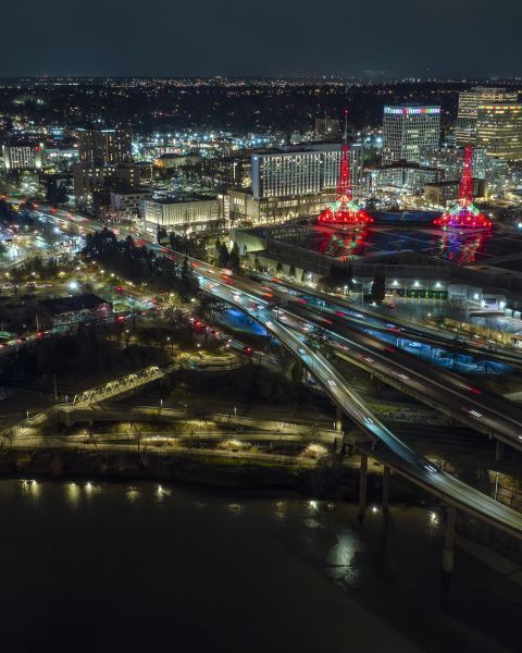 a night time aerial view of Portland\'s Convention and Moda Centers with traffic on the freeways spanning the river