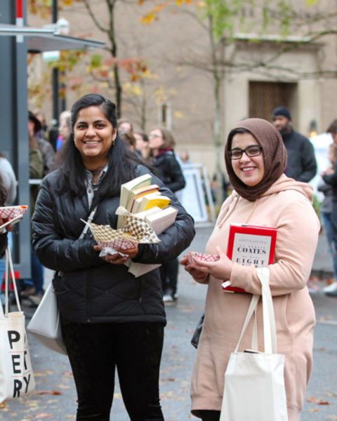 two people standing near a food cart carrying books