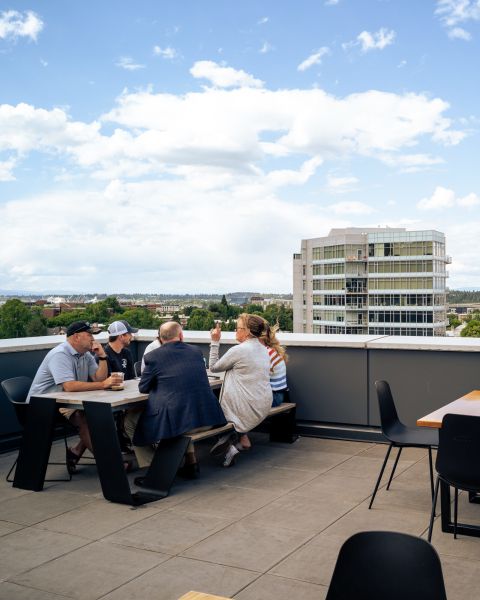 a group of people enjoy drinks on a rooftop bar patio overlooking the city