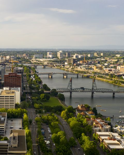 aerial view of downtown area with buildings and roadways, bridges crossing a river to a smaller set of buildings that expand into the distance