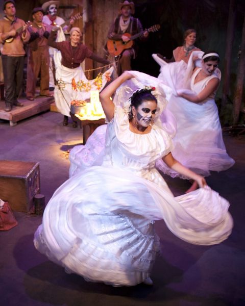 Actors dancing across a stage in long white dresses and skeleton makeup