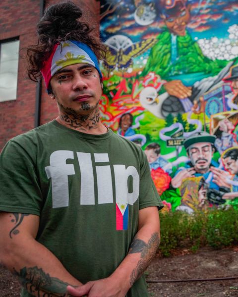 Talilo Marfil, wearing the flag of the Philippines as bandana and a shirt with the word, \'flip,\' (a slang term for Filipino) stands in front of a colorful mural depicting his likeness.
