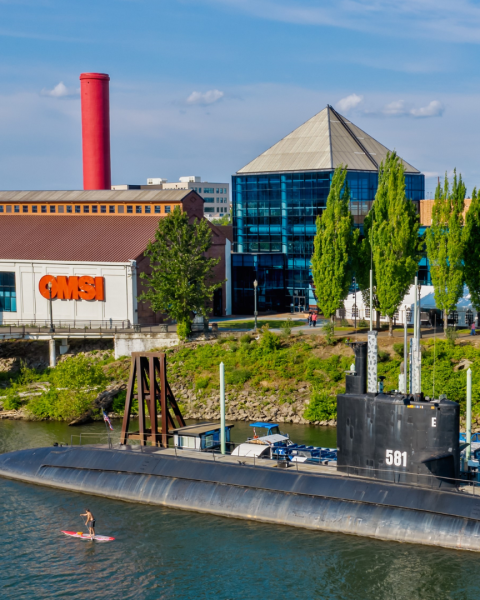 the exterior view of OMSI beside the Willamette River with a submarine docked by a pier.