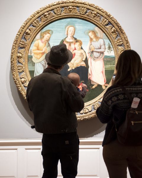 two people and a baby stand in front of a round oil classical painting of a religious scene at the Portland Art Museum