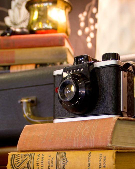 a vintage camera and suitcase displayed along with old hardcover books