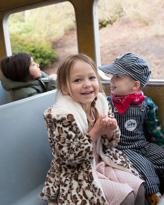 two children sitting on a train, one is dressed like a train conductor