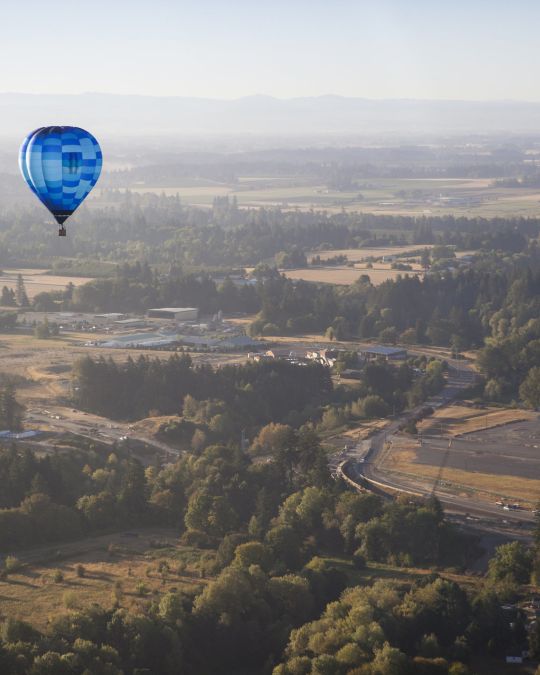 A hot air balloon floats above a wooded valley.
