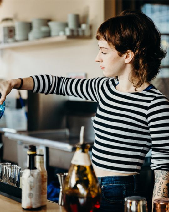 a bartender behind the bar pouring drinks from a blue bottle
