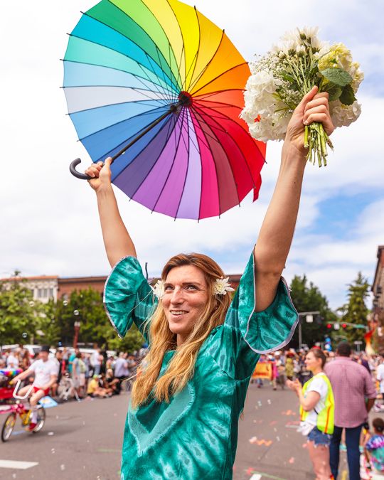 person holding up bouquet of flowers and rainbow flag during parade in a street parade