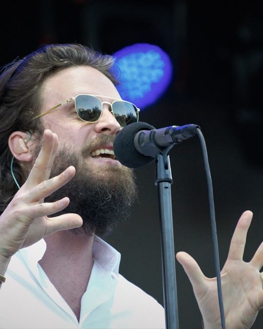 a bearded singer wearing sunglasses emotes into a microphone