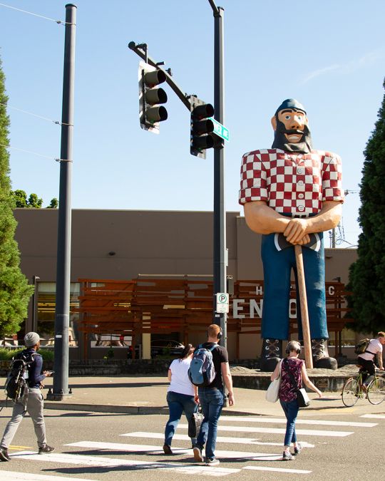 People cross the street in front of a 31 foot tall statue of Paul Bunyan