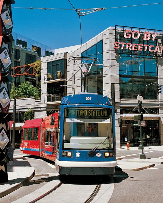 A streetcar passes by a large, red sculpture in front of a building with a neon sign reading, \"Go By Streetcar\"