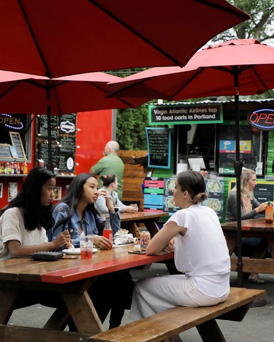 diners eating at a picnic table at an outdoor food cart pod