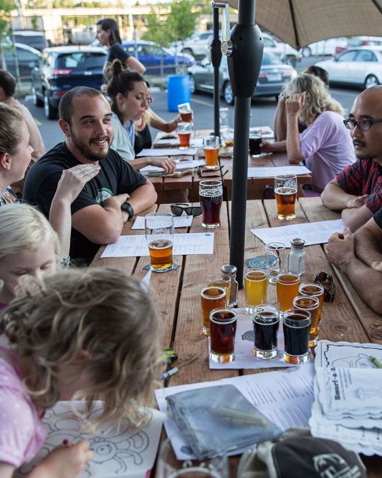 people of all ages around a picnic table covered with draft beers and coloring books