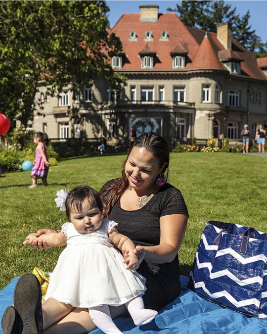Woman and child sit on picnic blanket on the lawn outside of Pittock Mansion