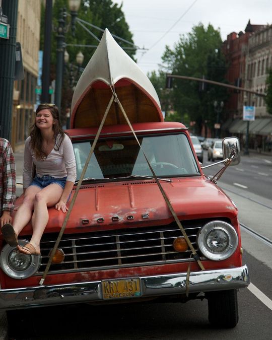 two people next to an orange truck with a canoe strapped to the top