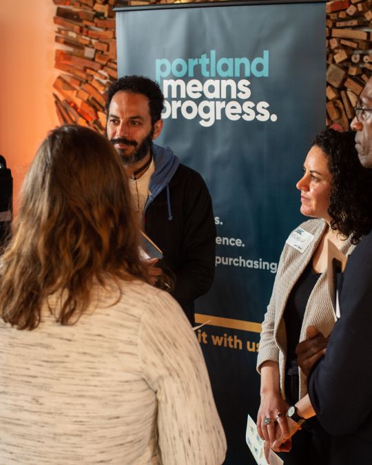 Business professionals gathered in a small group near Portland Means Progress banner