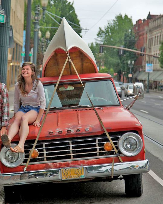 two people next to an orange truck with a canoe strapped to the top