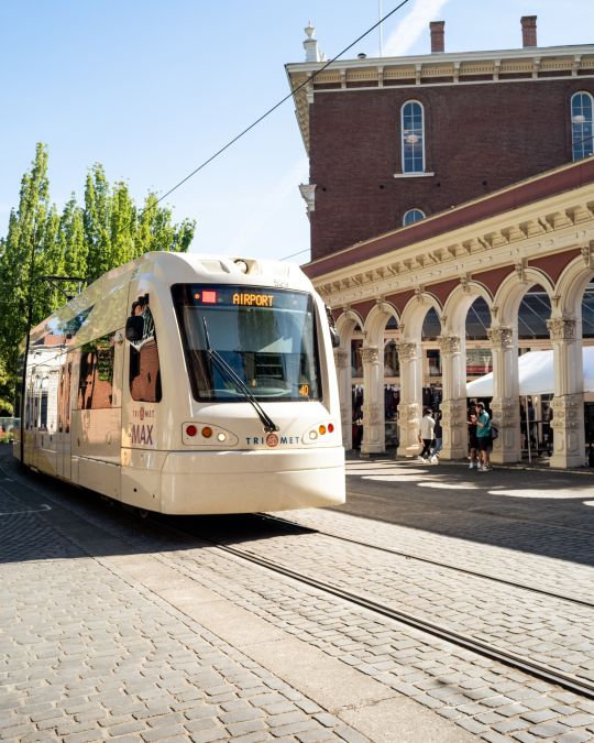 Light rail train car driving past people shopping at an outdoor market
