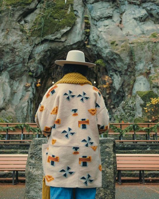 Someone stands in front of a rock wall.