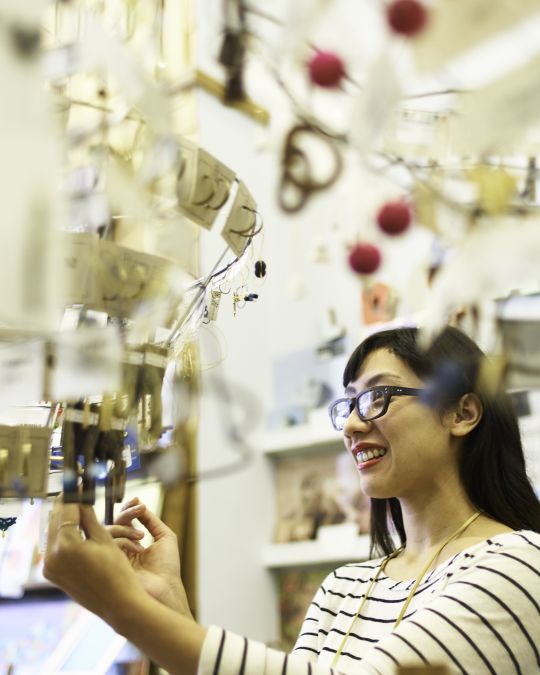 person with black glasses in striped shirt looks at earrings on a hanging jewelry display