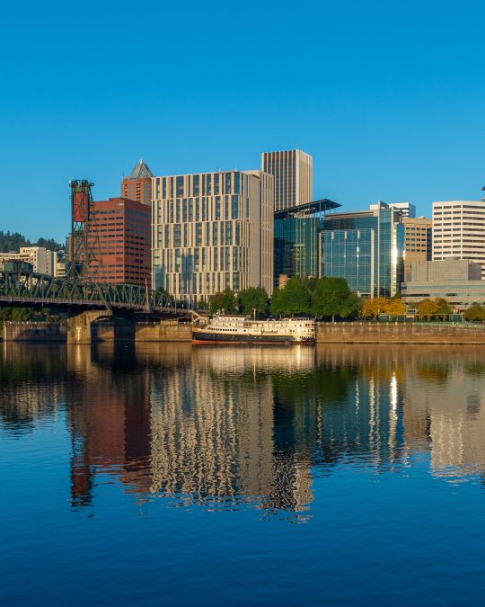 calm river water reflects the buildings in a downtown area that are catching the sunrise on a clear day
