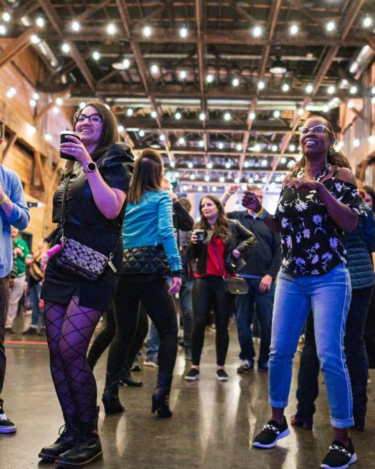 young people stand with drinks in their hands, string lights above in chic venue