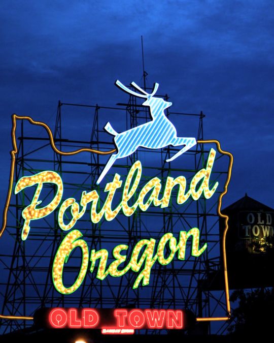 a neon light sign reading \"portland oregon old town\" with a deer leaping over the words
