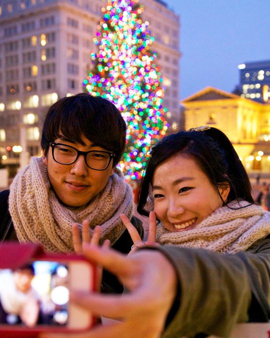 two people taking a selfie in front of portland\'s christmas tree