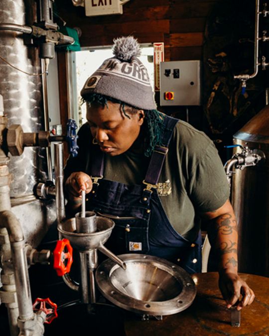 a brewer checks on a liquor she\'s distilling