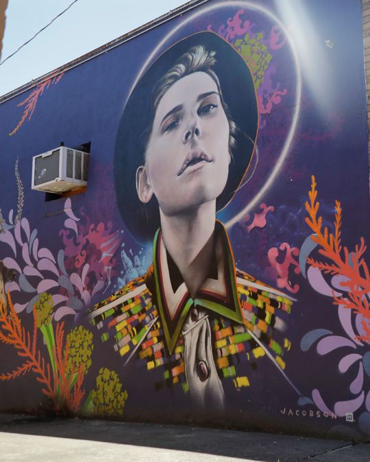 a multicolored mural depicting a person in a hat is painted on the side of a brick building
