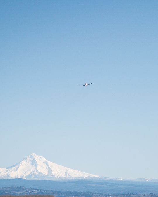 a plane takes off through clear blue skies with a snowy mountain in the distance