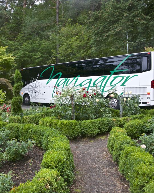 a large white motorcoach parked amid lush gardens in Washington Park