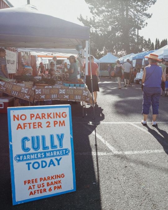 a parking lot filled with farmers market vendors, and a sign for the cully farmers market