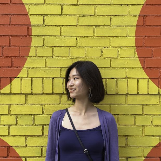 an image of a person in purple standing in front of a yellow wall with red polka dots