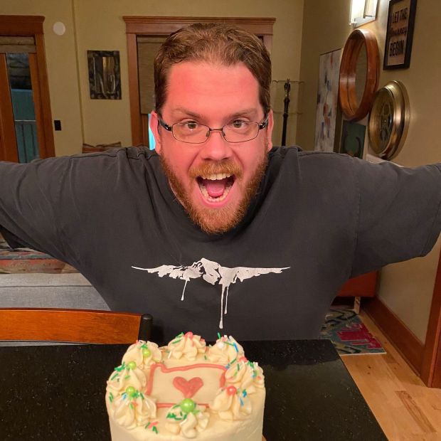 close up of a person with their arms outstretched in front of an ornately frosted cake