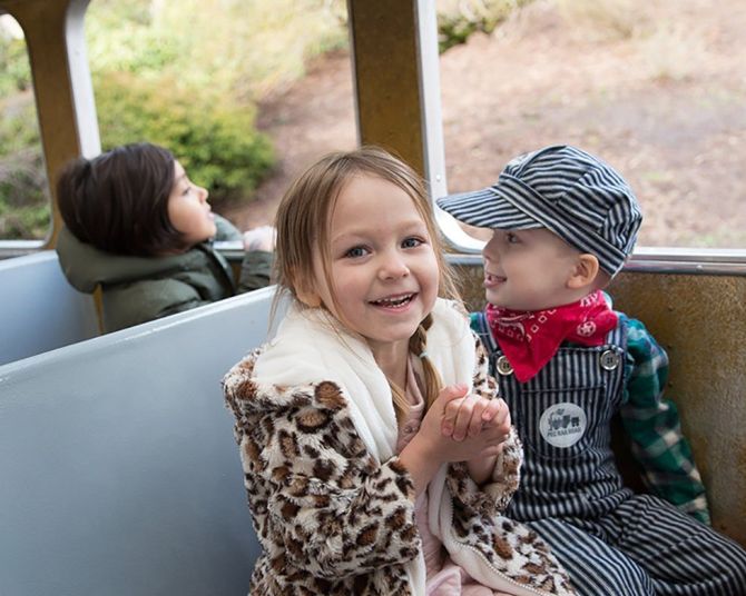 two children sitting on a train, one dressed like a train conductor