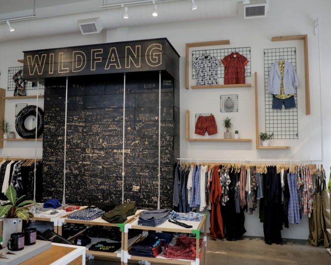 clothing on racks and folded on tables and large display with handwritten words