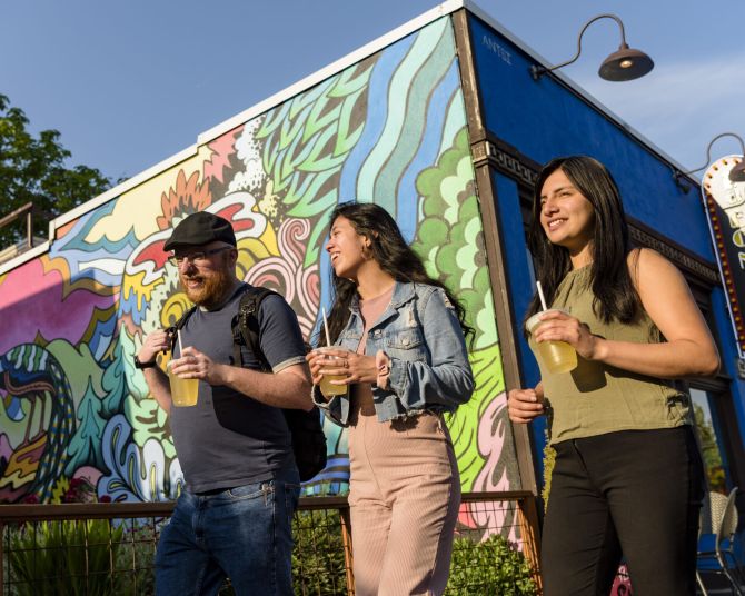 walking toward the sun, three people pass a colorful mural painted on the side of a building