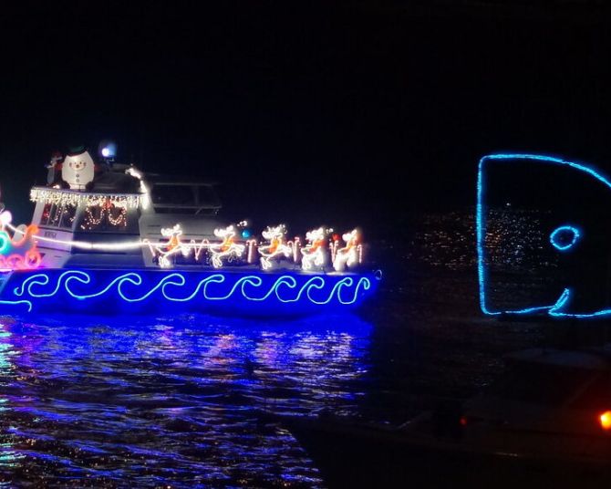 two boats on a river adorned with Christmas lights, one decorated to look like a blue whale