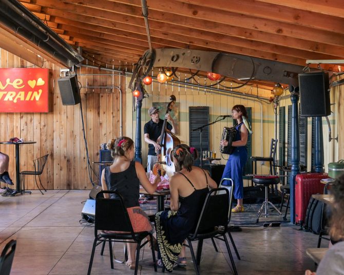 covered outdoor patio with stage and a band singing and playing accordion and upright bass for people seated at tables