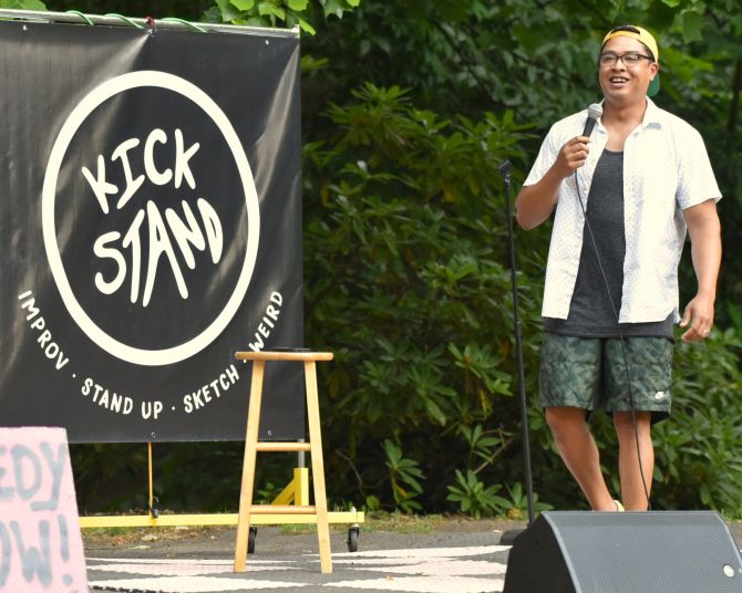 Comedian in a Ballcap performing on a stage set up in a park