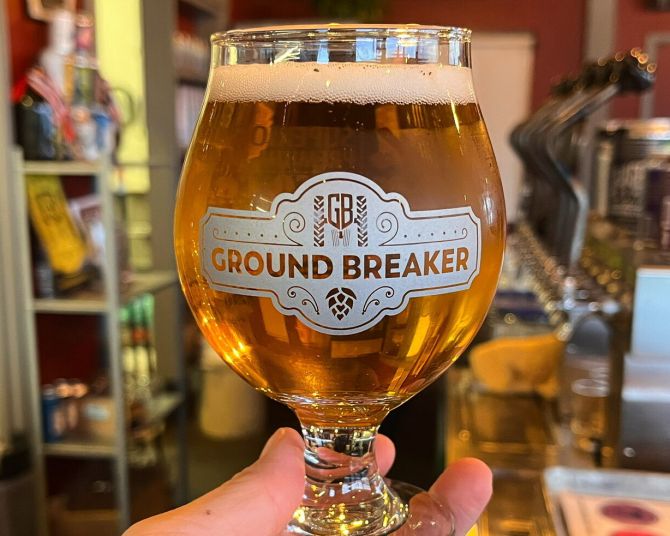 a hand holds a gluten free beer in a glass that says Ground Breaker Brewing on it