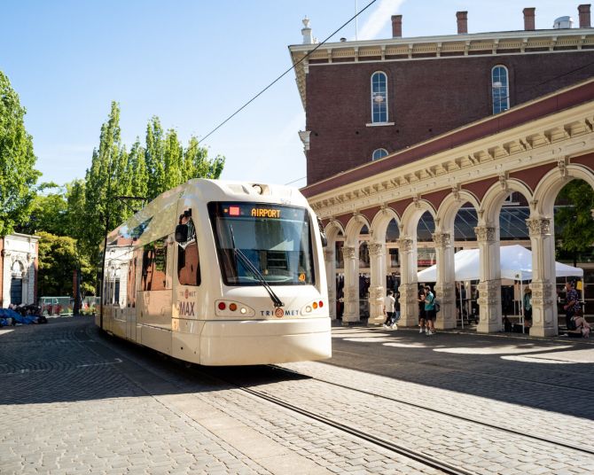 a light rail train on a cobblestone road passes the historic Saturday Market entry arches