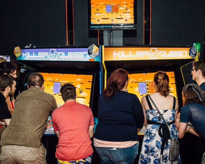 a group of people surround a large multi-player arcade game called Killer Queen