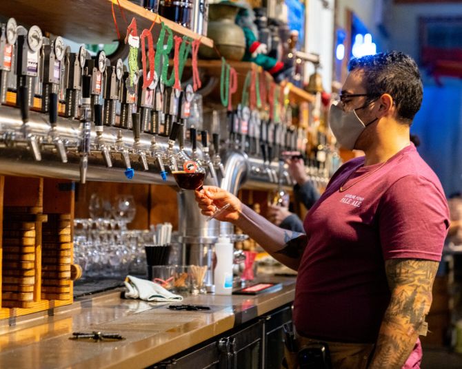 a person pours a dark draft beer from a long line of taps